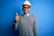 © Krakenimages.com - Young handsome african american engineer man with dreadlocks wearing safety helmet doing happy thumbs up gesture with hand. Approving expression looking at the camera showing success.