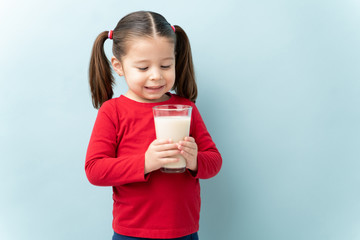 Wall Mural - Pretty little girl enjoying a glass of milk and smiling in a studio