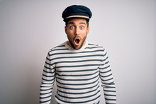 Young Handsome Sailor Man With Beard Wearing Navy Striped Uniform And Captain Hat Afraid And Shocked With Surprise Expression, Fear And Excited Face.