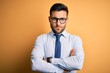 © Krakenimages.com - Young handsome businessman wearing tie and glasses standing over yellow background skeptic and nervous, disapproving expression on face with crossed arms. Negative person.