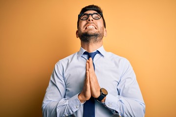 Wall Mural - Young handsome businessman wearing tie and glasses standing over yellow background begging and praying with hands together with hope expression on face very emotional and worried. Begging.