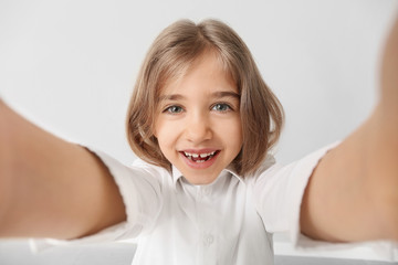 Wall Mural - Happy little girl with healthy teeth taking selfie on light background