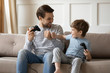 © fizkes - Overjoyed young father and little son sit relax on couch in living room playing computer games together, happy dad and small preschooler boy child celebrate win have fun enjoy family weekend at home