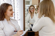 © Тарас Нагирняк - Optician is helping female client to choose glasses in optics, woman trying new glasses and looking at the mirror. Eye health care concept