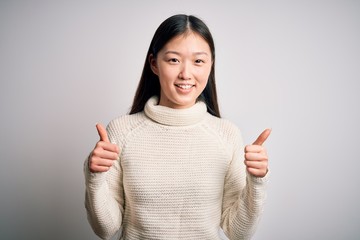 Young beautiful asian woman wearing casual sweater standing over isolated background success sign doing positive gesture with hand, thumbs up smiling and happy. Cheerful expression and winner gesture.