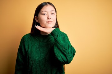 Canvas Print - Young beautiful asian woman wearing green winter sweater over yellow isolated background cutting throat with hand as knife, threaten aggression with furious violence