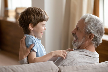 Wall Mural - Cute little boy relax in living room playing with excited elderly grandfather, overjoyed senior grandparent have fun engaged in funny activity with small grandson, enjoying time at home together