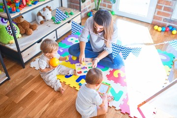 Poster - Beautiful teacher and toddlers playing around lots of toys at kindergarten