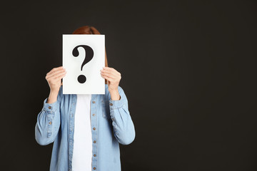 Woman holding question mark sign on black background. Space for text