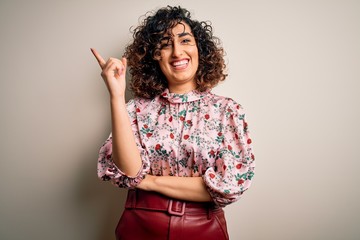 Poster - Young beautiful curly arab woman wearing floral t-shirt standing over isolated white background with a big smile on face, pointing with hand and finger to the side looking at the camera.