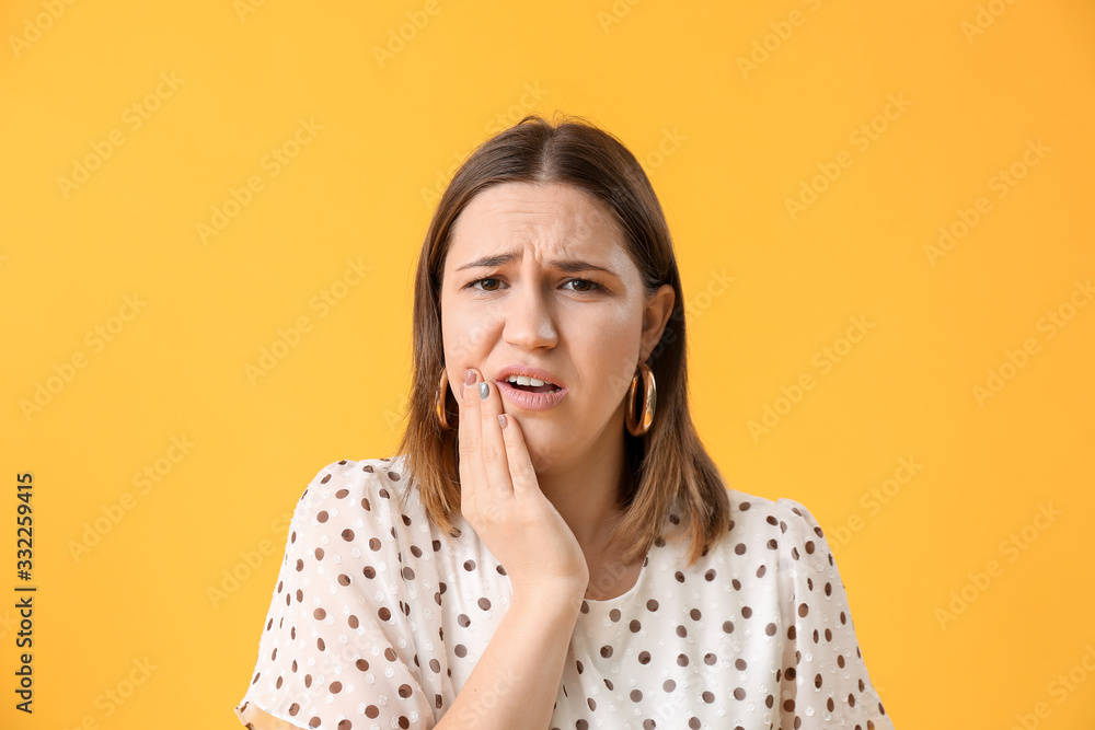 Young woman suffering from tooth ache on color background