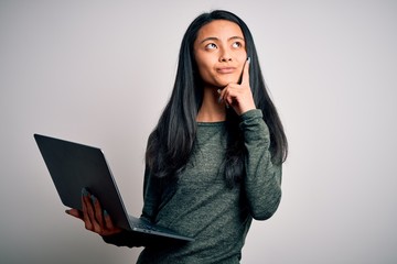 Wall Mural - Young beautiful chinese woman using laptop standing over isolated white background serious face thinking about question, very confused idea