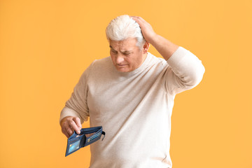 Poster - Sad senior man with empty purse on color background