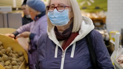 Wall Mural - Old woman in medical masks is shopping in the supermarket looking for the food