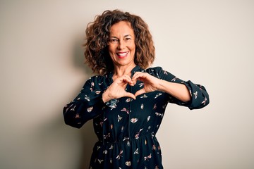 Wall Mural - Middle age beautiful woman wearing casual dress standing over isolated white background smiling in love showing heart symbol and shape with hands. Romantic concept.