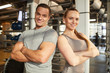 © Seventyfour - Waist up portrait of muscular couple smiling at camera while standing with arms crossed in modern gym lit by sunlight