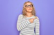 © Krakenimages.com - Beautiful blonde woman wearing casual striped t-shirt and glasses over purple background Pointing with hand finger to the side showing advertisement, serious and calm face