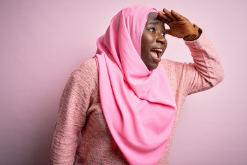 Canvas Print - Young african american plus size woman wearing muslim hijab over isolated pink background very happy and smiling looking far away with hand over head. Searching concept.