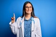 © Krakenimages.com - Young beautiful doctor woman wearing stethoscope and glasses over blue background showing and pointing up with finger number one while smiling confident and happy.