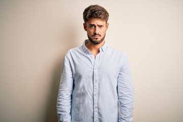 Wall Mural - Young handsome man with beard wearing striped shirt standing over white background skeptic and nervous, frowning upset because of problem. Negative person.