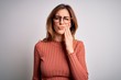 © Krakenimages.com - Young beautiful brunette woman wearing casual sweater and glasses over white background touching mouth with hand with painful expression because of toothache or dental illness on teeth. Dentist