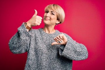 Sticker - Young blonde woman with modern short hair wearing casual sweater over pink background Doing thumbs up and down, disagreement and agreement expression. Crazy conflict