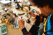 Improvement. Close Up Of Young Engineer Using Soldering Iron To Join Chips And Wires. Robotics And Software Engineering For Elementary Students. Inventions And Creativity For Kids