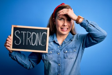 Poster - Young blonde woman holding blackboard with strong message over isolated blue background stressed with hand on head, shocked with shame and surprise face, angry and frustrated. Fear and upset