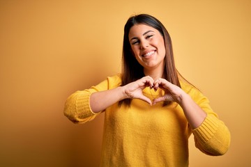 Canvas Print - Young beautiful woman wearing casual sweater over yellow isolated background smiling in love doing heart symbol shape with hands. Romantic concept.