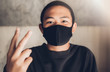© PAPALAH - The boy, wearing a black mask, covered his nose and mouth on his face, raising the two-finger symbol to indicate victory. Encouragement, fighting, smiling faces With bright eyes and hope.