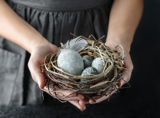 Woman hands holding marble Easter eggs with feathers on dark background with light. Happy Easter holiday, selective focus