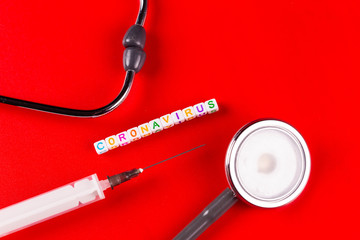 Pandemic and virus concept - Coronavirus text with syringe and phonendoscope on red background. Novel coronavirus Covid-19.