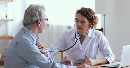 Wall Mural - Female doctor holding stethoscope examining old senior 60s grandpa patient in hospital. Cardiologist checking elderly man heartbeat at checkup medical visit. Older people cardiology healthcare concept