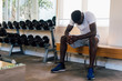 © twinsterphoto - Desperate African American male athlete sitting on bench during break in fitness training in modern gym