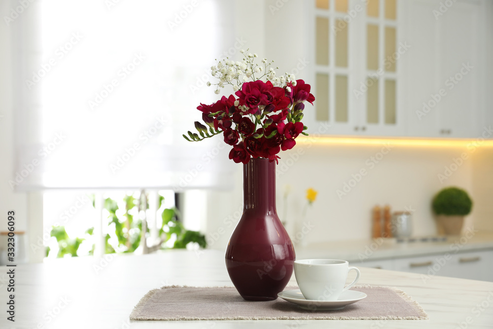 Beautiful bouquet with freesia flowers and cup on table in kitchen - obrazy, fototapety, plakaty 