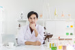 © Quality Stock Arts - Young Handsome Scientist sitting in laboratory working desk Asian race looking camera hand at chin