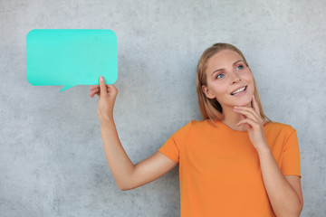 Beautiful young blonde woman standing isolated over grey background, holding empty speech bubble