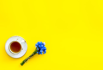 Poster - Summer tea party. Cup near cornflowers bouquet on yellow background top-down copy space