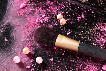 Wall Mural - A make-up brush with crushed cosmetics and pearls on a dark background, with a place for text