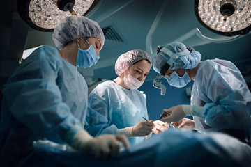 Medical team in the operating room, dark background. The theater of the operating room, an international team of professional doctors in a modern operating room are conducting an operation. Saving