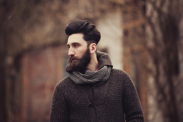 Young bearded man portrait. Sad elegant metrosexual male posing alone outdoor wearing knitted sweater.