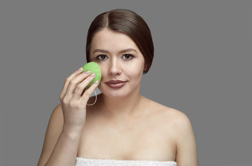 girl make a facial treatment with a green konjac sponge