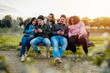 Group of young friends at the park playing with smart phones sitting on a bench at sunset - Generation z teens surfing on social networks together