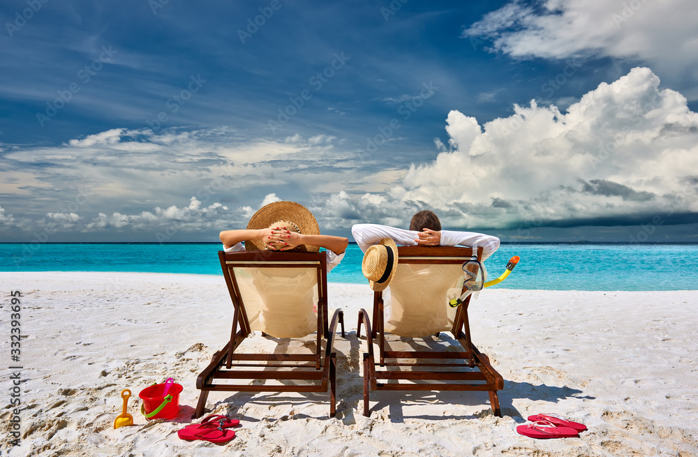 Couple in sun beds on a tropical beach - obrazy, fototapety, plakaty 