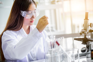 Attractive happiness scientist woman using microscope testing sample at laboratory with lab glassware. Science or medical research and development new antivirus or Covid-19 vaccine concept.