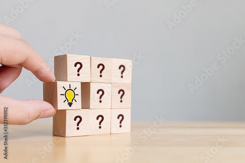 Conceptual of creative idea and innovation. Hand picked wooden cube block with head human symbol and light bulb icon and question mark symbol