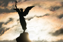 Silhouette Of An Angel With A Cross In His Hand On A Background Of Dramatic Sky And Sun. Fragment Of The Monument Mermaid , Installed In 1902 In The Kadriorg Park In Tallinn, Estonia.