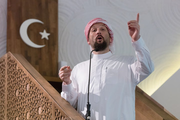 Poster - Muslims young arabic Imam has a speech on friday afternoon prayer in mosque. Muslims have gathered for the friday afternoon prayer in mosque and are listening to the speech of imam