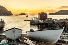 Small Fishing Boats Beached On A Wooden Ramp And A Small Boathouse And A Doc In The Background With The Setting Sun In The Distance