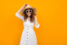Stylish Girl In A Straw Hat With Sunglasses Dressed In A White Dress On A Yellow Background With Copy Space